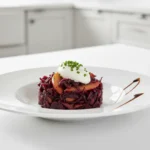 Recette Chou Rouge braisé dressé en cercle avec pommes et crème, décoré de ciboulette, sur une assiette blanche.
