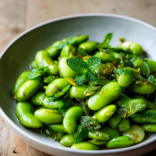 Gros plan sur des grains de fèves verts assaisonnés à la menthe et à l’huile d’olive dans un bol blanc