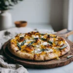 Pizza à la courge butternut maison sur planche en bois, garnie de mozzarella fondante, fromage de chèvre, oignons caramélisés et feuilles de sauge