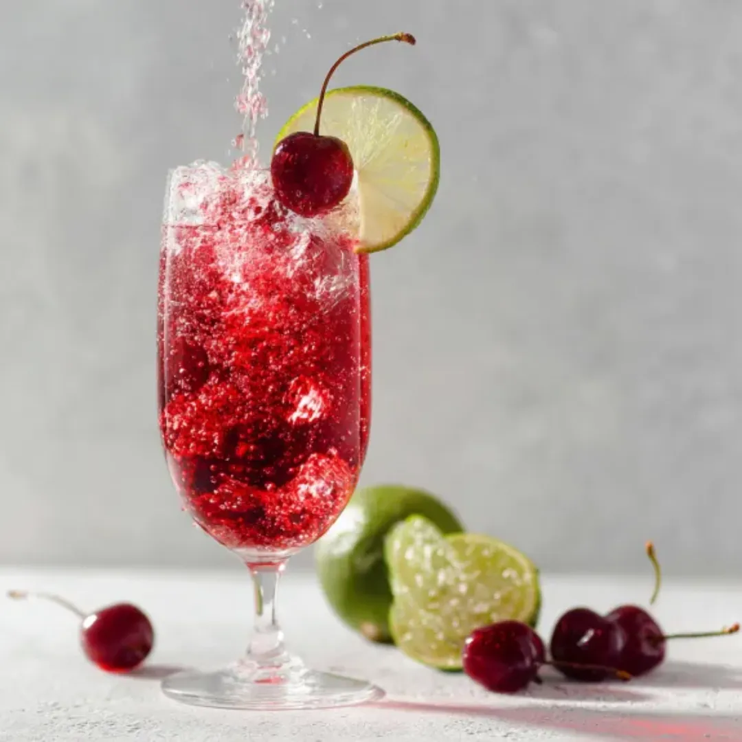 Vibrant le cocktail shirley being poured into a glass with cherries.