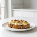 Tartine de chèvre miel noix servie chaude sur une tranche de pain grillé, garnie de fromage de chèvre fondant, de miel doré et de noix croquantes, dans une cuisine blanche lumineuse.